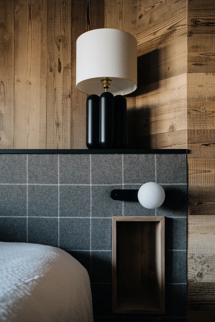 Lampe Charlotte de Cosin en gros plan et posée sur une tête de lit feutrée dans une chambre ambiance montagne remplie de bois chaud.