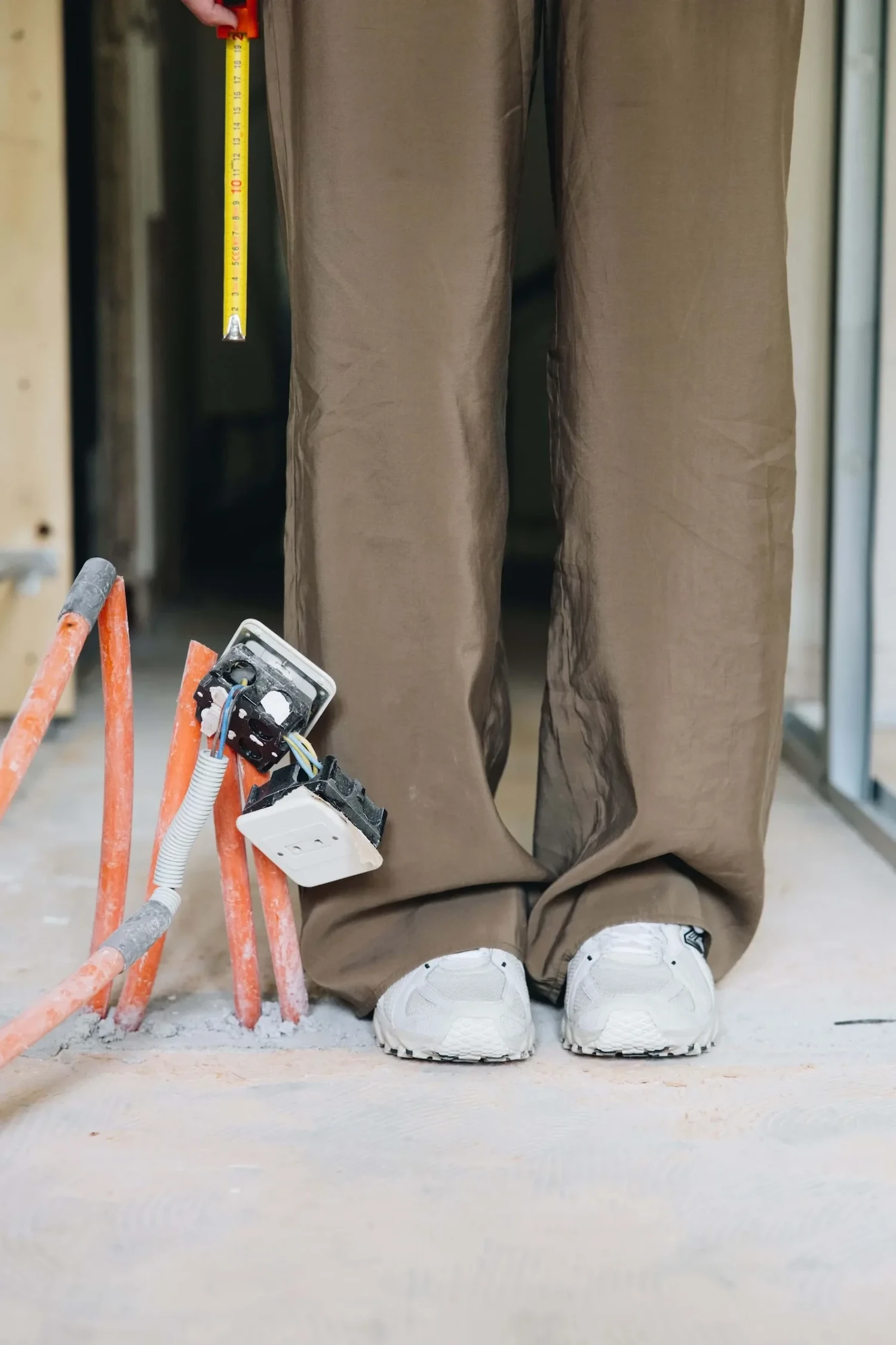 Portrait en gros plan de gaines d’électricité sur un chantier avec le bas des jambes d’Émilie Joly-Pottuz, fondatrice d’InSide Interior Design, spécialisée dans la rénovation totale de biens à la montagne, à Megève et alentours.