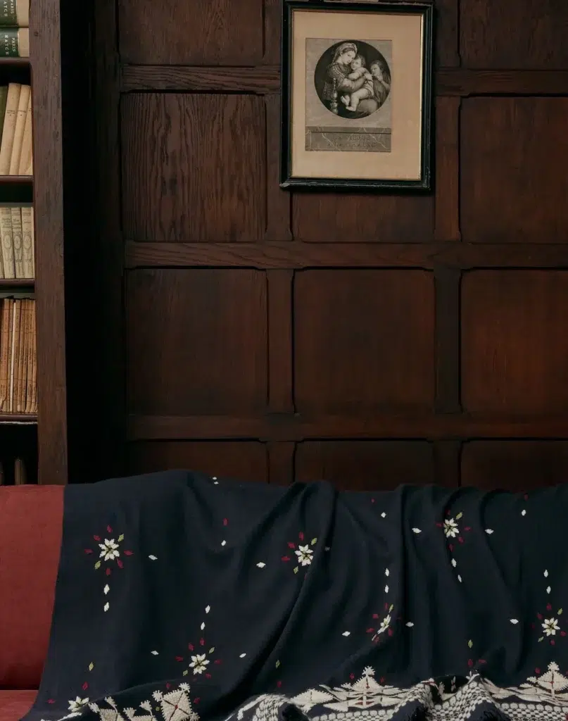  Plaid de la marque Caravane posée sur un canapé rouge sur fond de bois foncé.