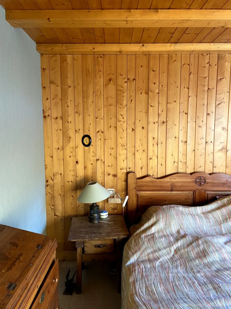 Une des chambres avant rénovation typique du style montagne avec du lambris en bois sur les murs et le plafond.