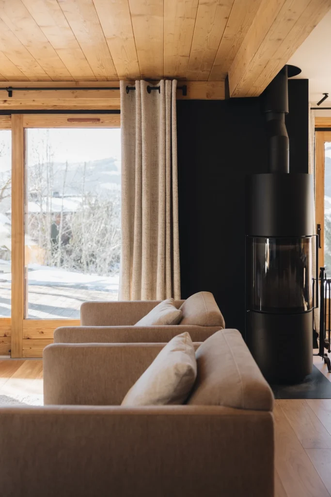 Nouveau salon moderne et aéré après rénovation complète de l’appartement. Vue du nouveau canapé, du nouveau poêle à bois et des paysages enneigés.
